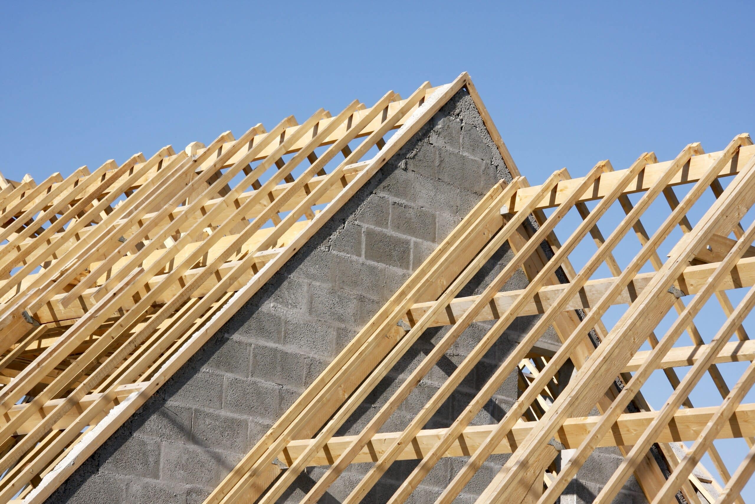 Charpente en bois neuve installée sur un pignon en parpaings gris sous un ciel bleu clair, illustrant une construction de toit.